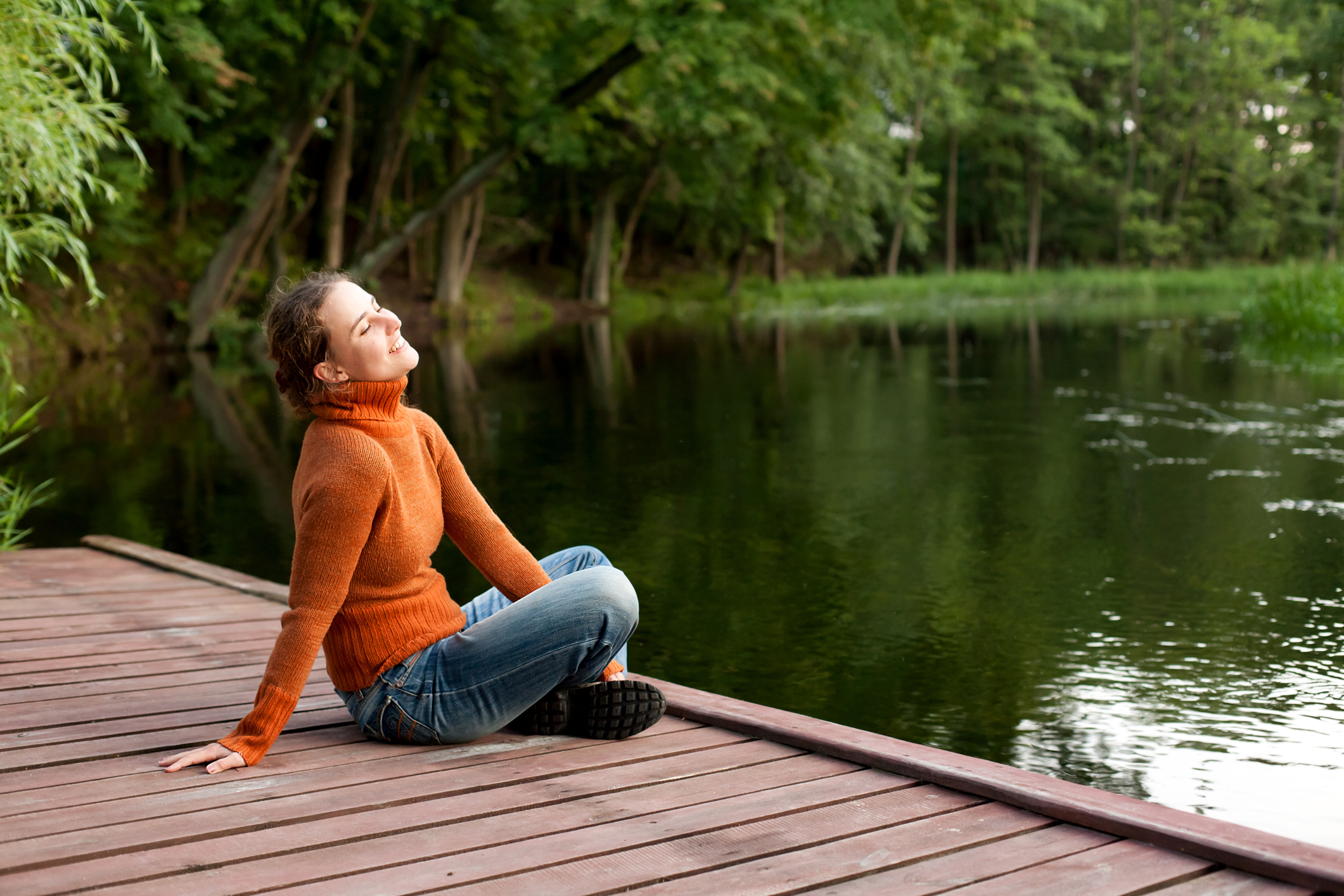 Woman in orange sweater relaxing on lakeside dock