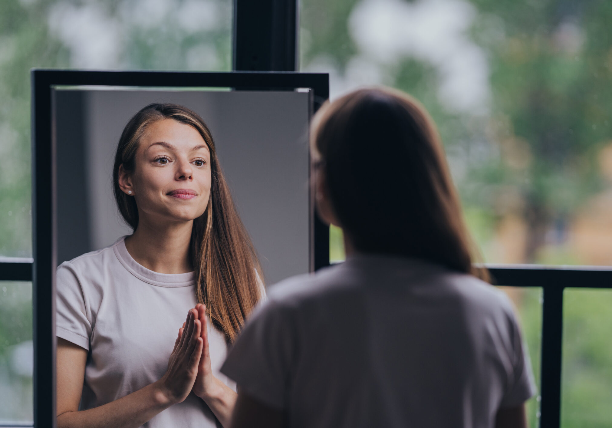 Woman meditating in front of a mirror with hands in prayer pose.